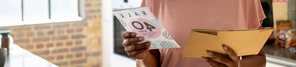 A woman reading a direct mail advertising piece promoting a sale.